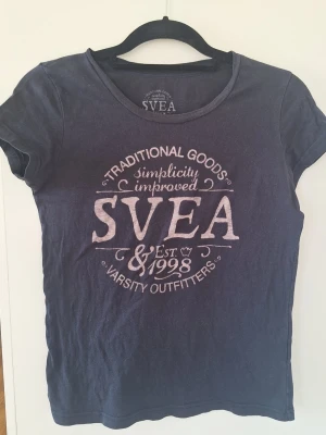 Mörkblå t-shirt från SVEA - Snygg mörkblå t-shirt från SVEA med tryck i vitt framtill. Klassisk rund halsringning och korta ärmar. Perfekt för en avslappnad och sportig stil. Tillverkad i mjuk bomull för skön känsla hela dagen.