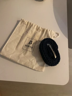 Boggi Milano flätat mocka bälte - Snyggt marinblått flätat bälte från Boggi Milano med silverfärgat spänne. Bältet har en klassisk design och levereras med en tygpåse med Boggi-logga. Perfekt accessoar för att lyfta din outfit. Inte lika basic som ett vanligt flätat bälte så perfekt för dig som vill sticka ut lite. Storlek 85 ~108 cm passar dig som vanligtvis kör 100 cm i ett vanligt bälte från t.ex. John Henric. Hör av er vid frågor och funderingar.