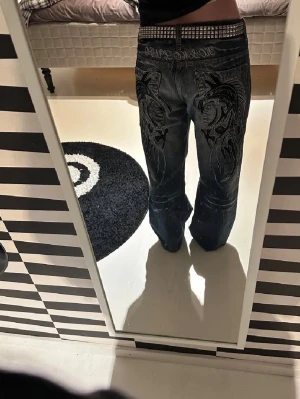 Baggy jeans med brodyr och tvättad look - Säljer ett par mörkblå baggy jeans med cool brodyr på bakfickorna och slitningar framtill. Jeansen har bred passform och låg midja, perfekt för en streetwear-stil. Materialet är klassisk denim och de har fem fickor.