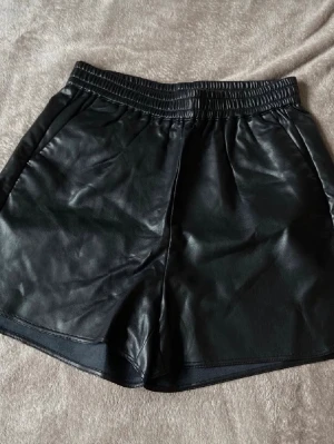 Skinn shorts  - Skinn shorts i läder imitation från Lindex, strl S, passar även M. Resår i midja. Helt nya, aldrig använda (dock hunnit tagit bort lappen) 