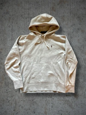 Beige hoodie från Polo Ralph Lauren - Snygg beige hoodie från Polo Ralph Lauren med klassisk huva och dragsko. Har en känguruficka framtill och den ikoniska lilla broderade loggan på bröstet. Tillverkad i mjuk bomullsblandning som känns skön mot huden. Perfekt för en avslappnad och stilren look.