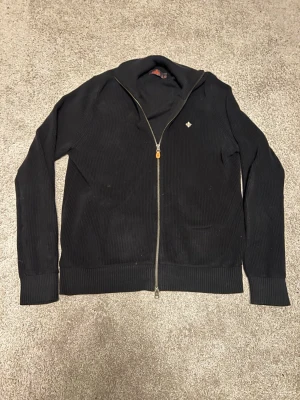 Svart ribbad ziptröja med emblem - Snygg mörkblå ribbstickad Morris  ziptröja, knappt använd, passar något större 