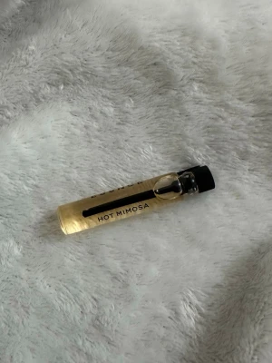 Hot Mimosa parfymprov essnce - Hot Mimosa parfymprov i en liten glasflaska med svart lock. Flaskan är genomskinlig med guldfärgad vätska och har enkel, stilren design. Perfekt att testa en ny doft eller ha med i väskan.