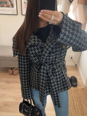 Rutig kappa med bälte - Snygg svart och grå rutig kappa med bälte i midjan och stora knappar framtill. Passar dig som gillar trendiga och tidlösa plagg. Skriv vid köp ☀️