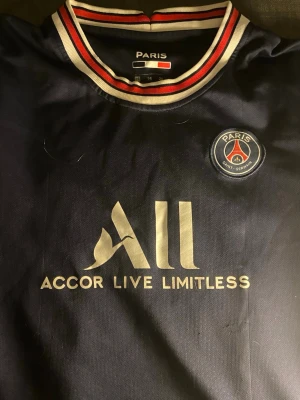 PSG matchtröja Messi #30 - Mörkblå PSG matchtröja med Messi och nummer 30 på ryggen. Tröjan har klubbmärke på bröstet, sponsorlogga 'Accor Live Limitless' och detaljer i vitt och rött vid kragen. Perfekt för fotbollsfans som vill visa sitt stöd för Paris Saint-Germain.