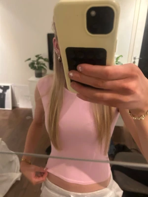 Ljusrosa croppad topp med öppen rygg - Säljer en ljusrosa croppad topp med öppen rygg och ärmlös design. Perfekt för dig som vill ha en enkel men snygg look. Toppens material är mjukt och stretchigt, vilket gör den bekväm att bära.