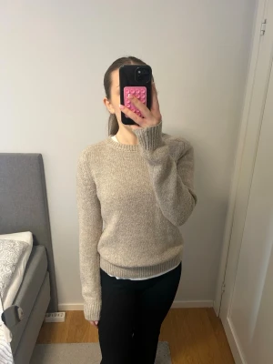 Beige stickad tröja med rund hals - Säljer en enkel och stilren beige stickad tröja med rund hals och långa ärmar. Tröjan har ribbstickade muddar vid hals, ärmslut och nederkant. Perfekt för lager-på-lager och passar till många olika outfits.