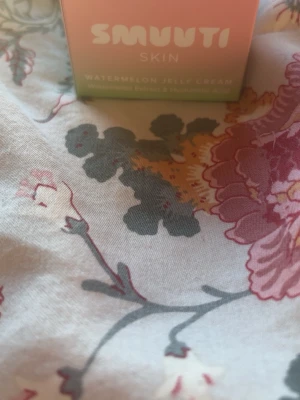 Smuuti Skin Watermelon Jelly Cream - En söt, pastellfärgad burk med Smuuti Skin Watermelon Jelly Cream. Denna ansiktskräm har en geléliknande konsistens och innehåller extrakt av vattenmelon samt hyaluronsyra för återfuktning. Perfekt för dig som vill ha en fräsch och lätt känsla på huden.