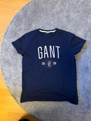 GANT t-shirt  - Snygg marinblå t-shirt från GANT med stort vitt tryck framtill och texten 'Open Road 49'. Klassisk rund halsringning och korta ärmar. Perfekt för en avslappnad och sportig stil.