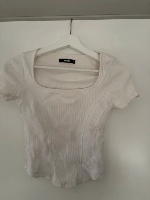 Vit ribbad topp från Bik Bok - Säljer en vit ribbad topp från Bik Bok med fyrkantig ringning och korta ärmar. Toppen har en figurnära passform och är tillverkad i ett mjukt, stretchigt material som passar perfekt till jeans eller kjol.