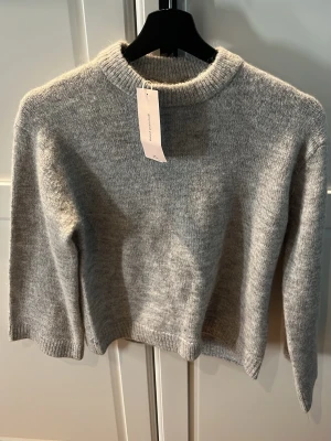 Grå stickad tröja från Gina Tricot - Mysig grå stickad tröja från Gina Tricot med rund halsring. Perfekt för lager-på-lager och enkel att matcha med jeans eller kjol. Klassisk och stilren design som funkar året runt. Helt oanvänd