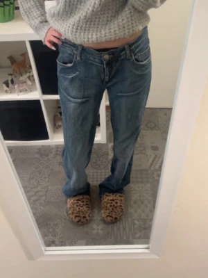 Blå bootcut lågmidjade jeans - Säljer ett par snygga blåa lågmidjade bootcut jeans med jätte fina fickor och mönster. Den har ett litet hål i slutet men det syns knappt. Den har även band inuti så man kan ändra midjan 💕jag är 163