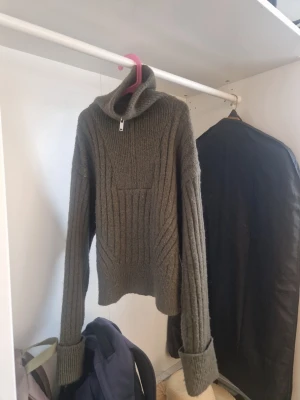 Olivgrön ribbstickad polotröja - Säljer en olivgrön ribbstickad polotröja med långa ärmar och breda muddar. Tröjan har en hög, mysig polokrage och är gjord i ett mjukt, tjockt material som passar perfekt när det är kallt ute. Enkel men snygg design som är lätt att matcha.