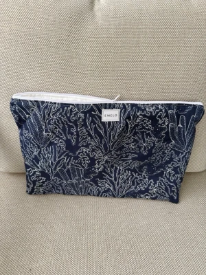 Blå datorväska med korallmönster Emelo - Snygg datorväska från Emelo i marinblått tyg med vitt korallinspirerat mönster. Väskan har dragkedja upptill och är perfekt för att bära din laptop eller surfplatta. Tillverkad i slitstarkt tyg och har en stilren, modern look. Passar laptop med maxmått: 33x24cm