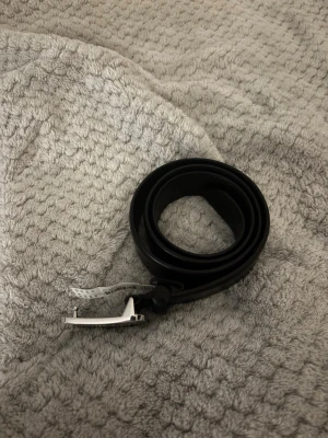 Morris bälte - Snyggt svart skärp från Morris med stilren, silverfärgad metallspänne där loggan är ingraverad. Bältet är i läder och storlek 100. Oanvänt. 