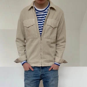Beige - Jeans overshirt - Säljer en beige jeans overshirt i färgen beige. Skjortan är i bra skick förutom att ena knappen på ena ärmen har försvunnit men inget som syns. Hör gärna av er vid frågor elr funderingar!!