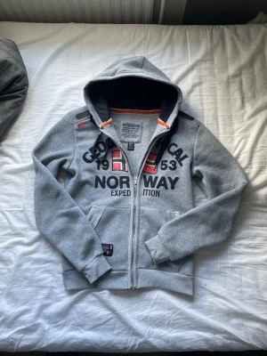 Grå hoodie från Geographical Norway - Snygg grå simpel zip hoodie från geographical Norway, väldigt slimmad look men sitter skönt ändå, passar från 175-185 skulle jag säga, hör av er med frågor osv✌🏼😌