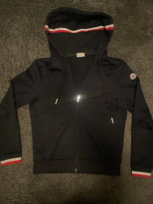 Moncler hoodie - Snygg svart hoodie från Moncler med zip. Storlek M men passar S ockps! Tröjan är i fint skick, inga skador. Kanske lite solblekt. Tveka inte på o fråga vid funderingar!🙌🏼
