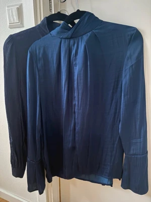 2 Mörkblå blusar - Två snygga mörkblå blusar med hög krage och långa ärmar.  Materialet ser ut att vara mjukt och följsamt, perfekt för att styla med jeans eller kjol. & Other Stories är i storlek 38 (den mönstrade) och Saint Tropez är i S 💞