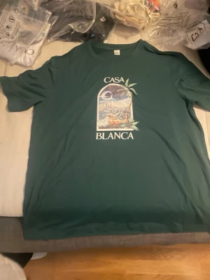 Grön Casa Blanca t-shirt - Snygg grön t-shirt från Casa Blanca med tryck framtill som visar ett tropiskt motiv och texten 'CASA BLANCA'. Klassisk passform och rund halsringning, perfekt för en avslappnad stil.
