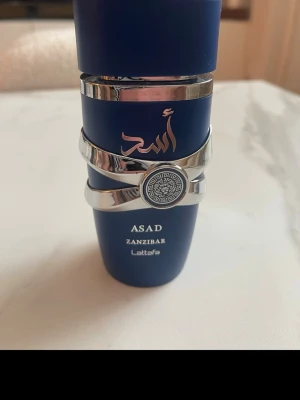 Lattafa Asad Zanzibar parfym & Revolution Man - Två parfymer: Lattafa Asad Zanzibar i en matt mörkblå flaska med silverdetaljer och orientaliskt mönster, samt Revolution Man i en stilren, helsilverfärgad flaska. Båda har modern design och passar dig som gillar unika dofter och snygga flaskor.   120kr lattafa och 50kr för revolution 