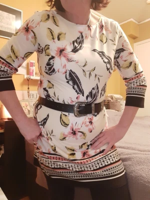 Blommig retro-style kortklänning med 3/4-ärm - Snygg kortklänning i vitt med stora blommor i rosa, svart och grönt. Klänningen har trekvartsärmar och dekorativa bårder vid ärmslut och nederkant. Skön passform och lätt material, perfekt för vår och sommar.