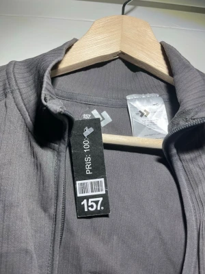 Mörkgrå ziptröja från 157 - Snygg mörkgrå ziptröja från 157 med hög krage och hel dragkedja framtill. Tröjan har en enkel, stilren design och är tillverkad i ett mjukt, stretchigt material som passar perfekt till vardags. Perfekt att slänga på sig över en t-shirt.