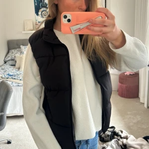 Svart dunväst med hög krage - Snygg svart dunväst med hög krage och quiltad design. Västen har en rak passform och stängs med dragkedja framtill. Perfekt att slänga över en hoodie eller stickad tröja för extra värme. Enkel och stilren look som passar till det mesta. Passar ca M till våren❤️