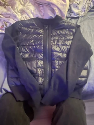 Gina tricot cardigan - Säljer en svart cardiganjacka med quiltad framsida och två stora fickor. Jackan har dragkedja framtill, ribbade muddar och ärmar i mjukt tyg. Perfekt för lager-på-lager och en stilren look.