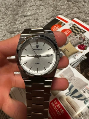 Silverfärgad klocka från Poedagar - Stilren klocka från Poedagar med silverfärgad urtavla och metallarmband. Klockan har tydliga markeringar, dag- och datumvisning samt quartz-urverk. Klassisk design som passar till många olika stilar.