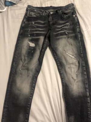 Svarta slitna jeans från Jack & Jones - Säljer ett par svarta jeans från dsquarden 2 med slitningar och distressed detaljer på både fram- och baksida. Jeansen har en smal passform och klassisk femficksdesign. Materialet är bomullsdenim med stretch för extra komfort.