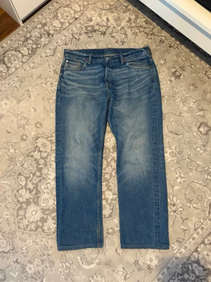 Blå raka jeans med vintage tvätt - Säljer ett par klassiska blå jeans med rak passform och snygg vintage tvätt. Jeansen har fem fickor, normal midja och subtila slitningar framtill. Perfekta till en avslappnad stil och tillverkade i mjukt denimtyg.