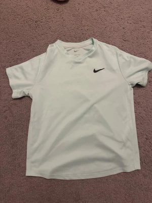 Ljusgrön/turkos Nike Dri-FIT t-shirt - Snygg ljusgrön/turkis t-shirt från Nike med Dri-FIT-teknologi som håller dig torr under träningen. Klassisk passform med rund hals och korta ärmar. Diskret Nike-logga i svart på bröstet. Perfekt för sport och aktivitet. Storlek 147-158, passar för ex en 12 åring. 