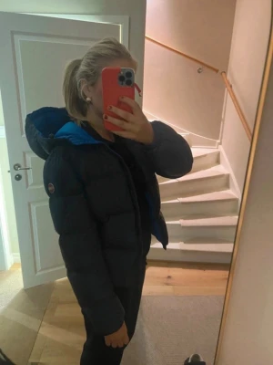 Mörkblå pufferjacka från Colmar - Säljer en riktigt snygg mörkblå pufferjacka från Colmar med blått foder och huva. Jackan har två dragkedjefickor, Colmar-logga på ärmen och en boxig, puffig passform. Perfekt för kalla vinterdagar och riktigt trendig look.