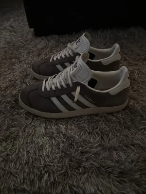 Archive Adidas Gazelle special edition - Säljer ett par klassiska Adidas Gazelle sneakers i grå/blå mocka med vita detaljer och vita. Skorna är lite använda men fortfarande i bra skick. Låg modell med retrovibe, perfekt för dig som gillar stilrena och tidlösa sneakers. Storlek 38,5. Colorway på denna är limited och svår att hitta.  Hör av er vid funderingar😃