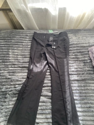 Svarta utsvängda kostymbyxor - Snygga svarta kostymbyxor med utsvängda ben och pressveck. Byxorna har fickor fram och bak, samt hällor för skärp. Perfekta för en stilren look och passar till många olika outfits.