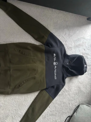 Grön och blå hoodie från Sail Racing - Snygg hoodie från Sail Racing i grön och blå färg med stor logga på bröstet. Klassisk känguruficka framtill och huva med dragsko. Tillverkad i mjukt och bekvämt material, perfekt för chill dagar eller när du vill ha en sportig look.