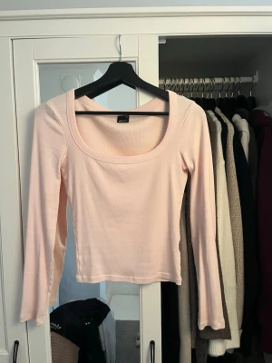 Ljusrosa ribbad topp Gina Tricot - Säljer en ljusrosa långärmad topp från Gina Tricot i ribbat material. Toppen har en djup, rundad urringning och är figurnära i modellen. Perfekt att matcha med jeans eller kjol för en enkel och snygg look.