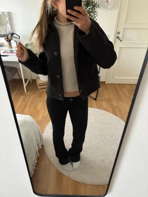 Svart kortare vårjacka - Säljer en svart, kort jacka med stora knappar framtill. Jackan har en boxig passform och är långärmad, perfekt för att ge en cool och enkel look. 