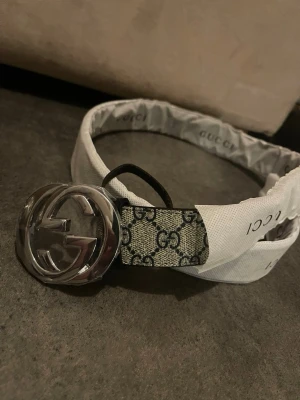  GG bälte med silverfärgat spänne - Snyggt bälte  med klassiskt GG-mönster i svart och beige. Bältet har ett stort, silverfärgat GG-spänne som verkligen sticker ut. Perfekt accessoar för att lyfta vilken outfit som helst.