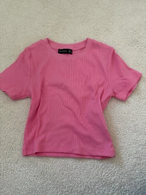 Rosa ribbad t-shirt från Barres and Oil - Säljer en rosa ribbad t-shirt från Barres and Oil. T-shirten har korta ärmar, rund halsringning och en croppad passform. Perfekt för dig som gillar en enkel men ändå trendig stil.