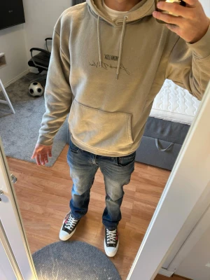 Beige hoodie med Mona Lisa-tryck - Snygg beige hoodie från pull n bear med tryck framtill och stort Mona Lisa-motiv på ryggen. Hoodien har huva med dragsko och en stor magficka. Perfekt för dig som gillar streetwear och unika prints.