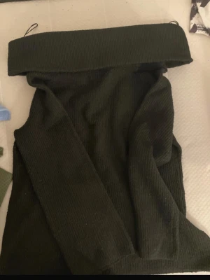 Svart ribbad offshoulder topp - Trendig svart  ribbad offshoulder topp med bred krage. Toppen är ärmlös och har en croppad passform som passar perfekt till höga jeans eller kjol. Materialet är mjukt och stretchigt för en bekväm känsla.