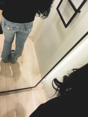 Ljusblå bootcut jeans med fickdetaljer - Säljer ett par ljusblå bootcut jeans med snygga fickdetaljer bak och dekorativa knappar. Jeansen har låg midja och är tillverkade i klassisk denim. Perfekta för en trendig och avslappnad look.