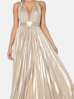 Champagnefärgad långklänning med djup urringning - Elegant långklänning i skimrande champagnefärg med djup v-ringning och halterneck. Klänningen har ett brett midjeband och plisserad kjol, perfekt balklänning! Eftertraktad från bubbleroom, helt slutsåld.❤️ Inga skador, köpt för 1200!
