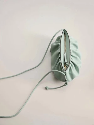 Ljusgrön axelväska/ dumpling bag - Trendig ljusgrön/ turkos  axelväska i mjukt konstläder med rynkad design och smal axelrem. Väskan har dragkedja upptill och dekorativa knutar på sidorna. Perfekt för dig som vill ha en stilren men unik accessoar. Nästan aldrig använd så Nyskick! Perfekt till sommaren!💓