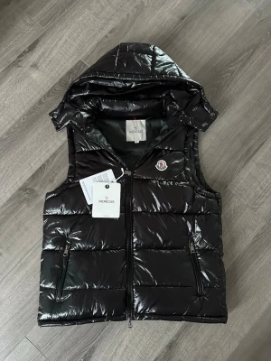 Svart moncler väst nfc - Säljer en Helt ny Svart Moncler väst från moncler.com perfekt väst till en fin och stilig outfit. Den är tunn och är perfekt nu inför våren och sommar kväll. Den har nfc så fort mobilen nuddar logon så kommer moncler.com upp direkt till västen. Storlek S 