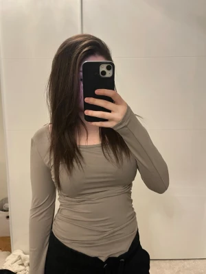 Beige långärmad topp i stretch - Säljer en beige långärmad topp med tight passform och rundad halsringning. Toppen är gjord i ett stretchigt material som sitter snyggt på kroppen och passar perfekt till både jeans och kjol. Enkel och stilren design utan mönster eller detaljer.