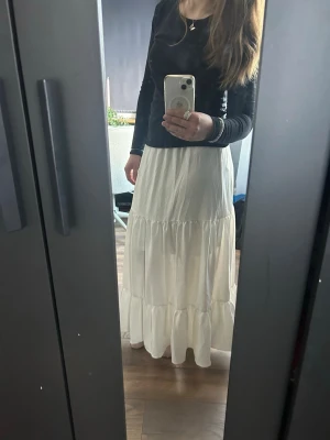 Vit långkjol från Cider - Säljer en vit långkjol från Cider med volangdetaljer. Kjolen har en luftig passform samt ett snitt i sidan av kjolen ( synd inte på bild)  Aldrig använd