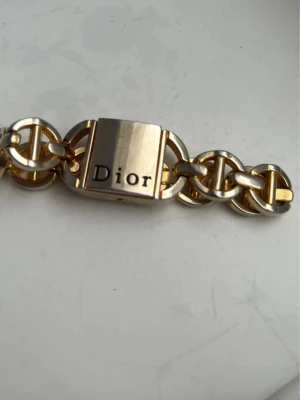 Guld- och silverfärgat Dior armband - Snyggt armband från Dior i guld- och silverfärgad metall. Länkarna är robusta och har en chunky design med en fyrkantig låsdetalj där Dior-loggan är ingraverad. Perfekt accessoar för att lyfta din outfit med en lyxig touch.